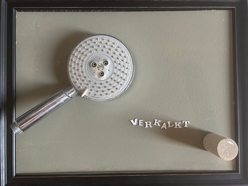 Michael Thomas Schröder, Verkalkt – shower head and the pasted letters “Verkalkt” on grey ground in a black frame